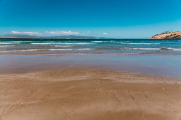pristine wild landscape at Clifton Beach in Tasmania, Australia with wavy blue ocean and golden sand next to a rugged coastline