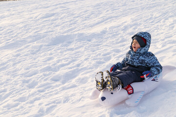 Young child sliding happily down a snowy hill on a toboggan