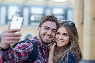 Happy couple of tourists taking selfie in showplace of city. Man and woman making photo on city background