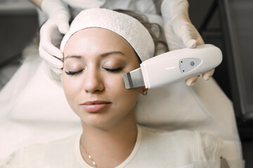 Naklejka premium beautician using an ultrasound device cleans the patient's skin