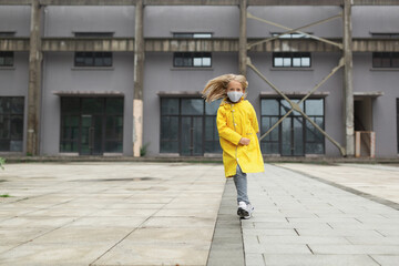 Obraz na płótnie Canvas little caucasian girl 7 years old with blonde hair in yellow raincoat and face mask during Coronavirus pandemic. Colors of the year 2021 ultimate gray and illuminating