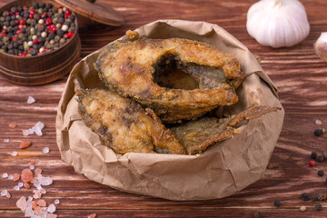 Pieces of fried carp in a paper bag on a wooden table. Food delivery