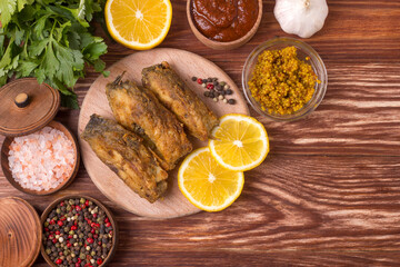 Pieces of fried carp on a wooden board with herbs, spices and lemon. Top view