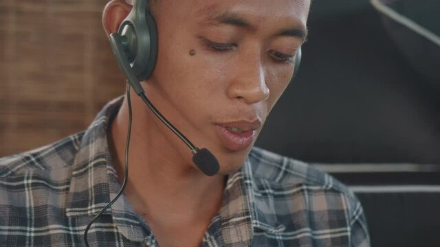 Close up of young Asian man wearing checkered shirt and headset having telephone consultationClose up of young Asian man wearing checkered shirt and headset having telephone consultationClose up of yo
