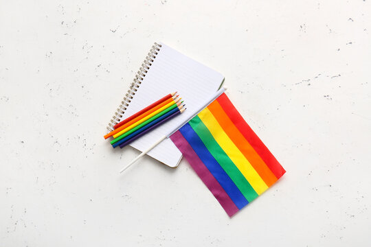 Rainbow LGBT flag, notebook and color pencils on light background
