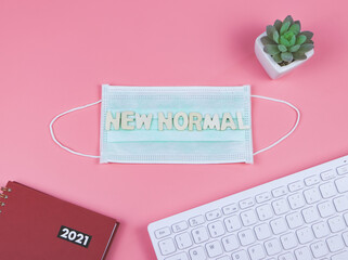 flat lay of wooden letters NEW NORMAL on medical face masks red 2021 planner ,succulent plant pot and computer keyboard on pink background. 2021 Planning, COVID-19 prevention and new normal concept.