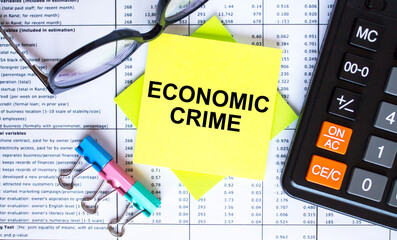 Text Economic Crime on yellow stickers with calculator, eyeglasses and paper clips