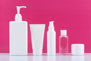 Body cream, face cream, cleaning foam, lotion and under eye cream on white table against bright pink background. Concept of set for skin and body care, hygiene or anti aging treatment