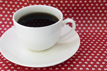 On a red background with hearts is a white cup of coffee.