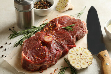 Baking paper with raw steak meat, herbs and spices on white textured background