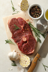 Baking paper with raw steak meat, herbs and spices on white textured background