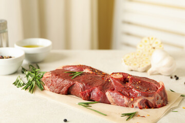 Baking paper with raw steak meat, herbs and spices on white textured background