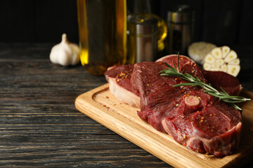 Spices, oil and board with raw steak meat on wooden background