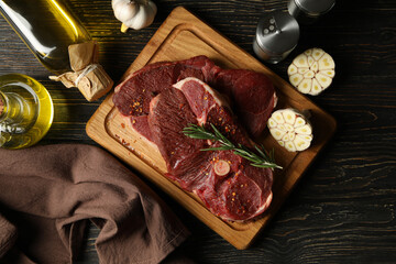 Spices, oil and board with raw steak meat on wooden background