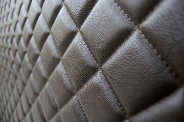 Fototapeta premium Stitched leather. Background of diamond-stitched leather, photo at an angle to the surface. Close-up photos, selective focus.