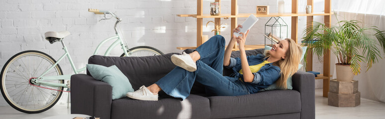  young woman looking at digital tablet during video call on couch at home, banner