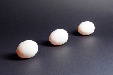 Eggs on a black background, three eggs in a row, shadow on the background of eggs, healthy and diet food.