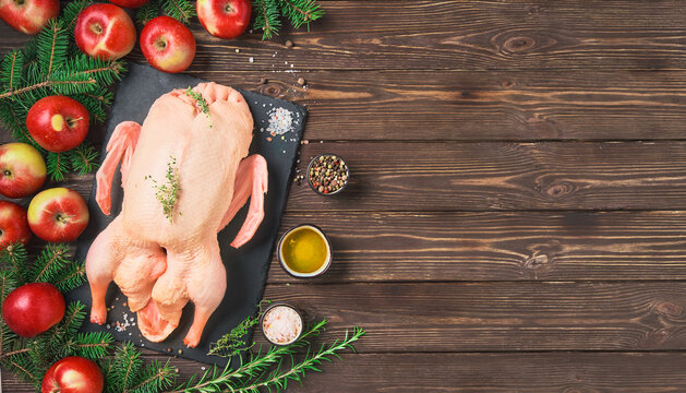 Raw duck in a baking sheet with apples and spices. Layout of ingredients on a wooden table. Recipe for making a festive dinner for Christmas or New Year. Top view with copy space