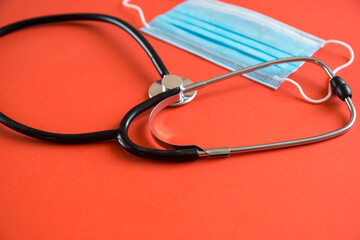 Close-up of a stethoscope and a medical protective mask on a bright orange background. Selective focus, shallow depth of field