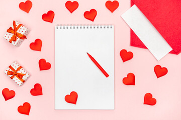 Flatlay notepad mock up with felt-tip pen with a red envelope with hearts and gifts on a pink background. Concept of valentine's day and writing love letters