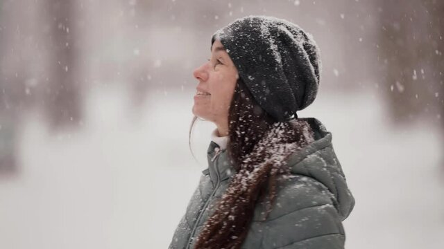 middle-aged woman is strolling outdoors at snowy winter day, snow is falling on her
