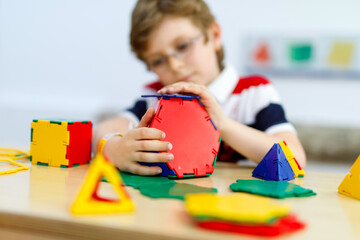 Happy kid boy with glasses having fun with building and creating geometric figures, learning...