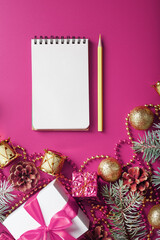 Notepad in holiday toys and decorations on pink christmas background.