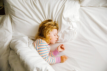 Cute little toddler girl sleeping in big bed of parents. Adorable baby child dreaming in hotel bed on family vacations or at home.