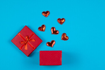 Opened gift box with red hearts on blue background. Flat lay