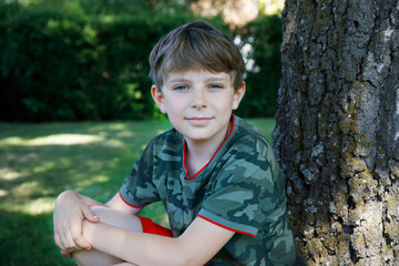 Outdoor portrait of happy smiling preteen kid boy on sunny summer day in park near tree. Handsome...