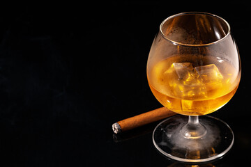 Glass of whisky and lighted cigar on black background