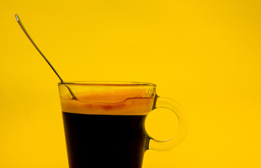 Coffee cup with spoon inside on yellow background with copy space.