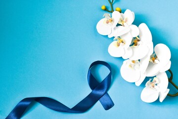 World cancer day. Flower orchid and blue ribbon on a blue background. World cancer day and medicine concept. Copy space, flat lay. Top view.