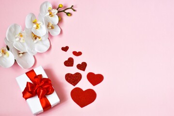 Valentine's Day card. Gift box, orchid flower and red hearts on a pink background. Valentine's Day, Mother's day background. Holiday concept. Copy space, flat lay. Greetings card.