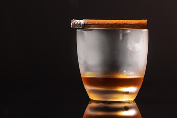 Burning cigar and glass of whisky on black background