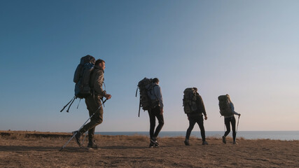 The four travelers with backpacks walking on the seascape background