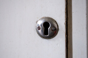 White old dirty scratched cupboard door with small silver round keyhole (with two small screws)