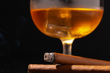 Glass of whisky and lighted cigar on black background