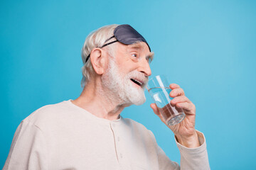 Fototapeta na wymiar Profile side photo of aged man pensioner drink water happy smile wear pajamas look empty space isolated over blue color background