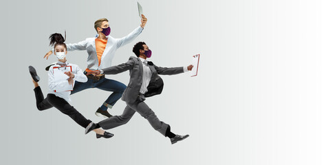 Happy office workers in face masks jumping and dancing in casual clothes or suit isolated on studio background. Business, start-up, prevention of COVID, motion and action concept. Creative collage.