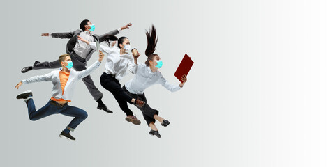 Fototapeta na wymiar Happy office workers in face masks jumping and dancing in casual clothes or suit isolated on studio background. Business, start-up, prevention of COVID, motion and action concept. Creative collage.