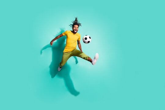 Full size photo of young smiling positive happy afro man jumping playing football isolated on teal color background