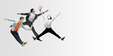 Fototapeta na wymiar Happy office workers in face masks jumping and dancing in casual clothes or suit isolated on studio background. Business, start-up, prevention of COVID, motion and action concept. Creative collage.