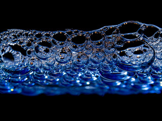 Makroaufnahme von Seifenschaum in weiss und blau, vor schwarzem Hintergrund.