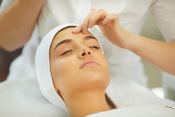 Fototapeta na wymiar Hands of cosmetologist checking skin elasticity or making facial cleaning for young relaxing woman