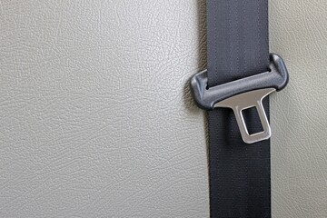 Buckle and strap of a car seatbelt against a pale cream blank leather background