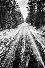 Asphalt road covered with snow leading through the forest. Winter scenery shown in black and white.
