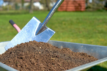 Shovel in fresh compost soil in a wheelbarrow  and a green background