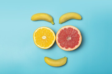 Tropical fruits summer background. Fruits face (bananas, oranges and grapefruits) on a colored blue background. Smoothie, summer vacation, sun and vitamins concept.