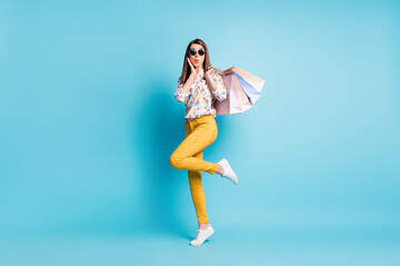 Fototapeta na wymiar Full length body size photo of surprised girl keeping bags after shopping wearing sunglass isolated on bright blue color background